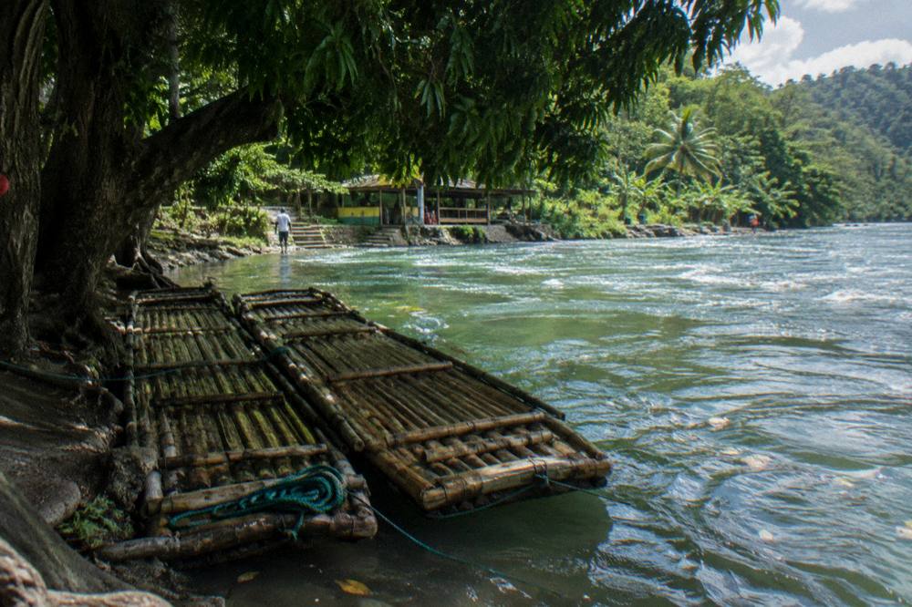 Two empty bamboo rafts resting side by side at a shaded river landing