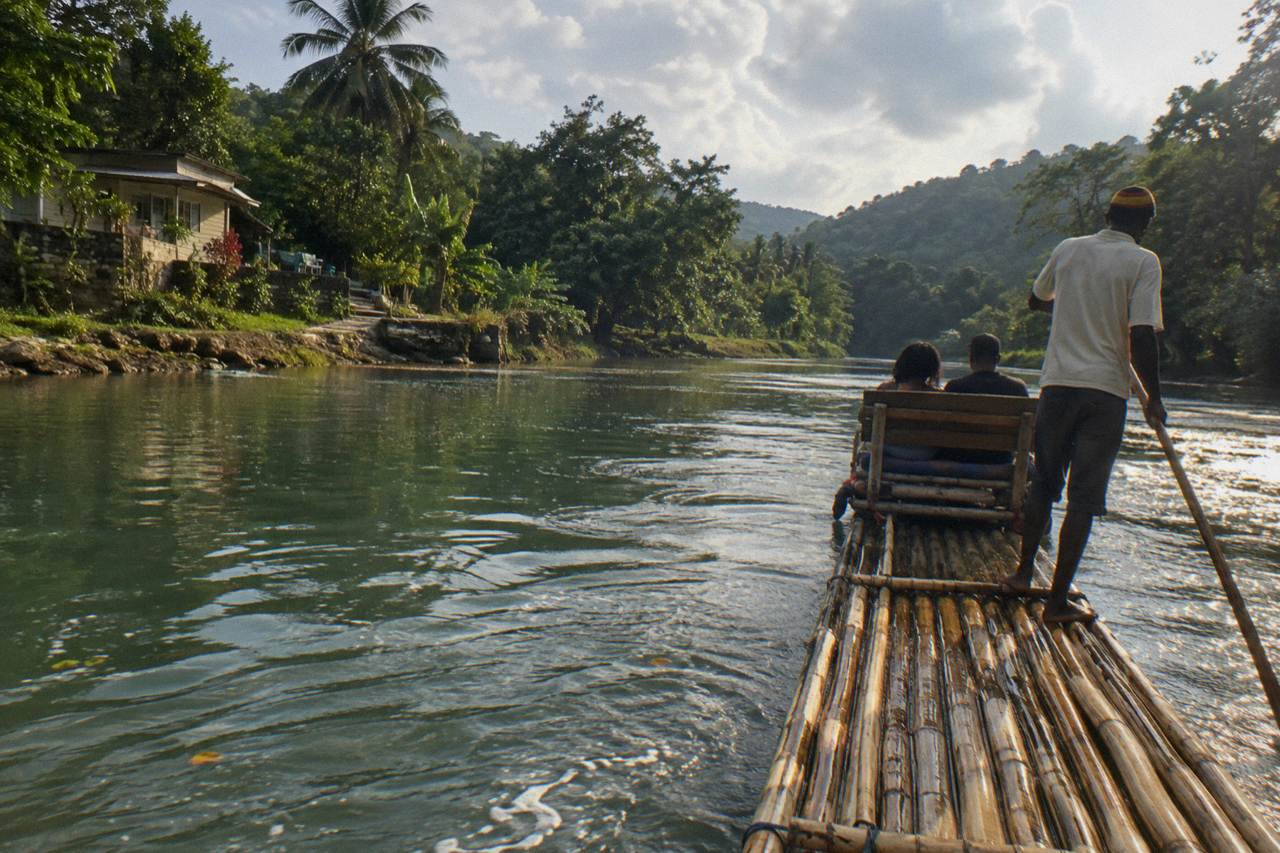 A long bamboo raft drifting on a calm green river between tree lined banks