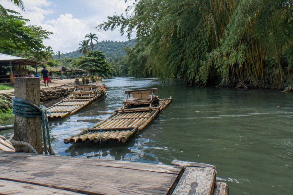 A wooden raft dock on a quiet riverbank with moored bamboo rafts in the background