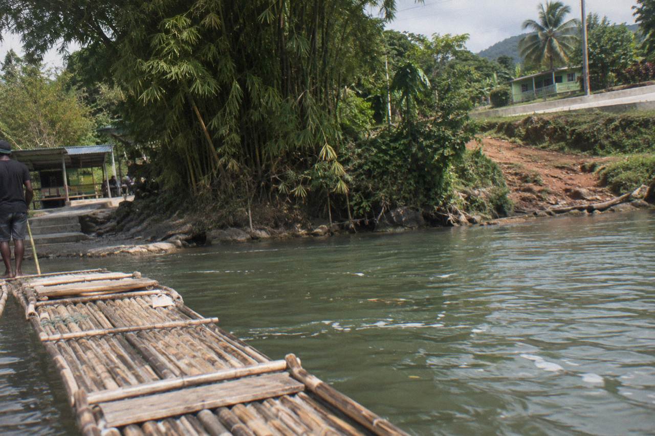 A long bamboo raft resting on calm green river water beside a dense tropical riverbank