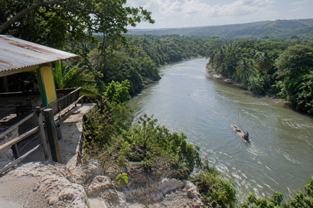 A wide calm river bending between dense green forested banks under a bright sky