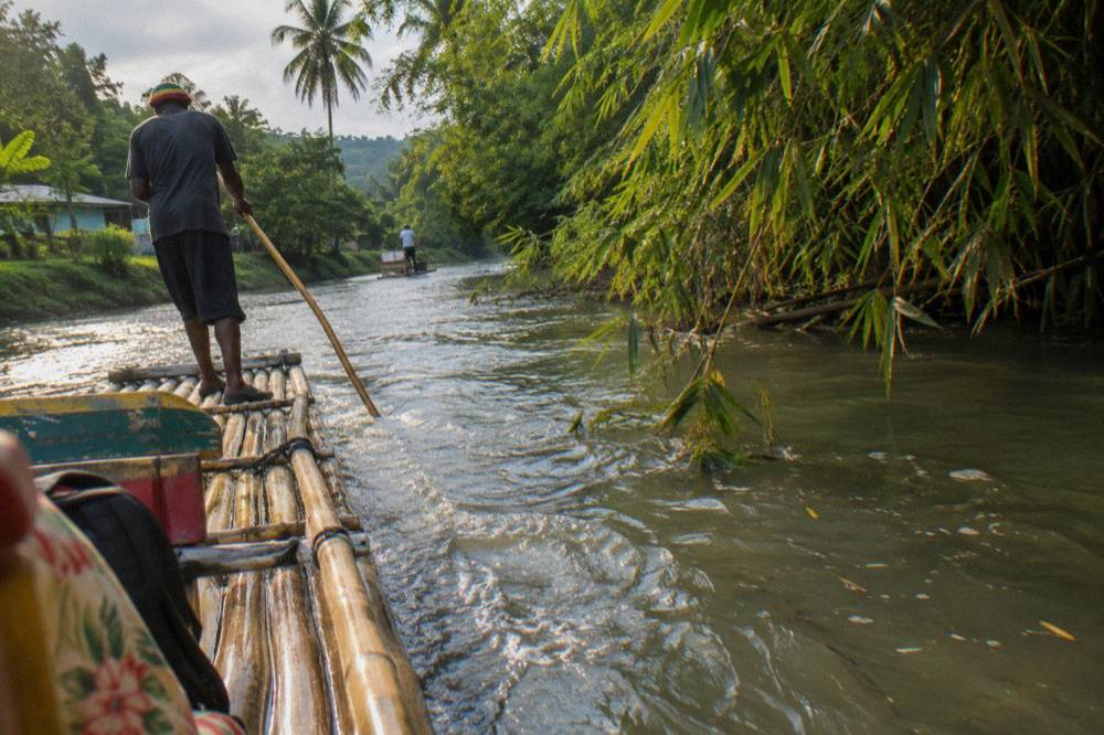 A bamboo raft captain poling the raft along a narrow green river corridor