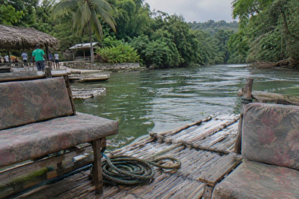 Two padded seats on a bamboo raft resting at a wooden riverside dock