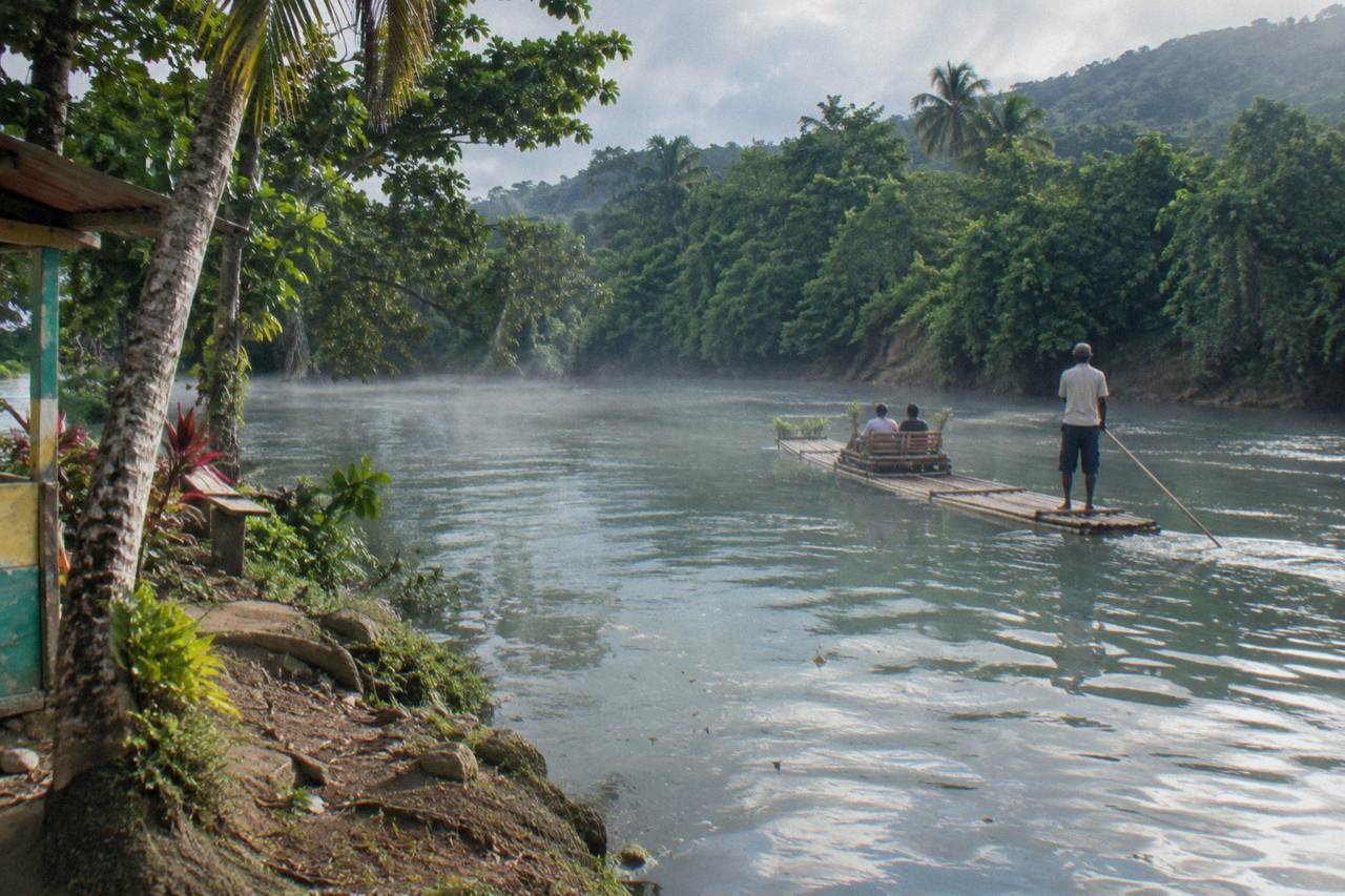A long bamboo raft drifting on calm green river water between tree-lined banks