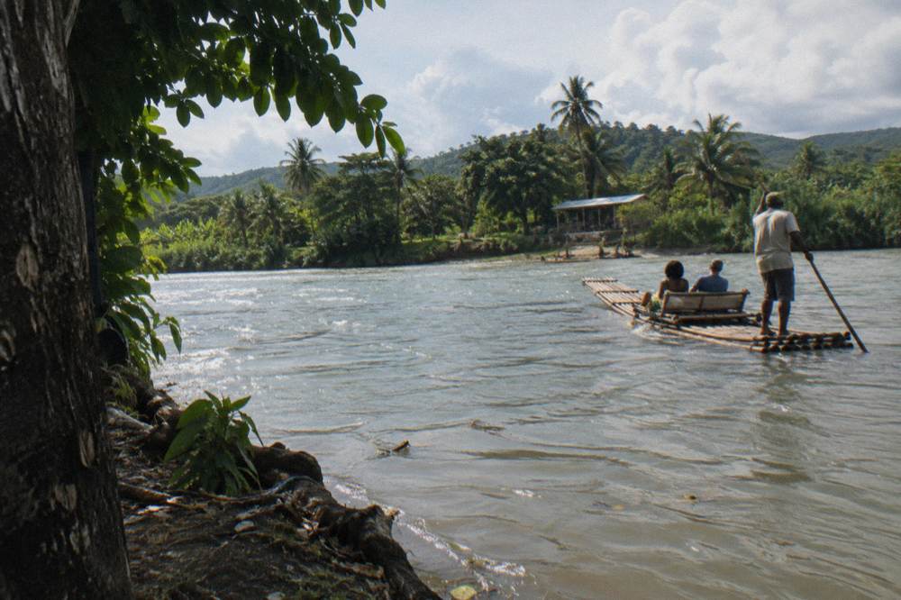 A raft captain steering with a long pole on a wide calm river