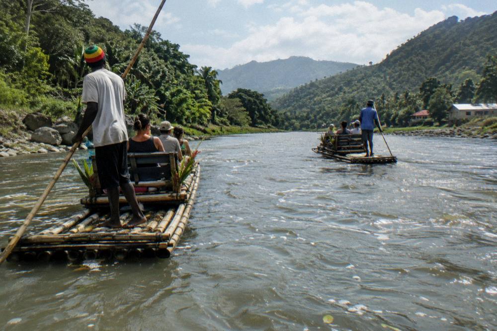 Two bamboo rafts floating side by side on a wide river between green hills