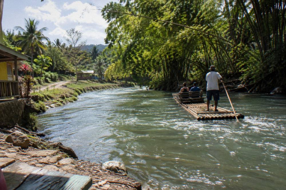 A quiet Jamaican river bend with bamboo stands along the bank under a bright sky