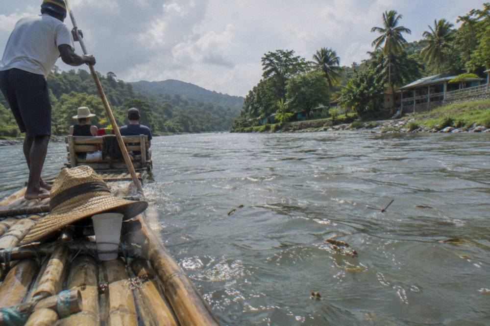 A wooden raft captain poling a bamboo raft along a wide calm river