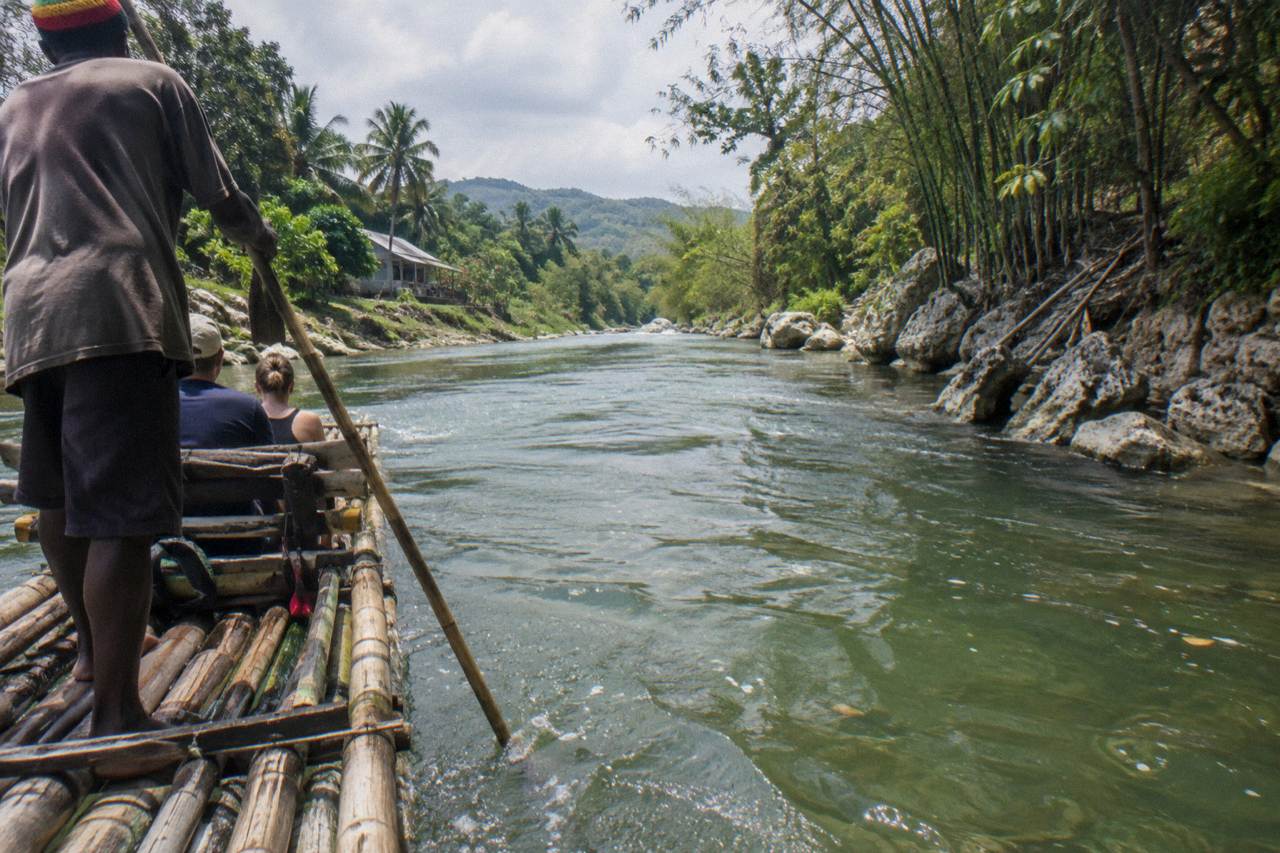 A long bamboo raft drifting on a calm green river between forested banks in Jamaica