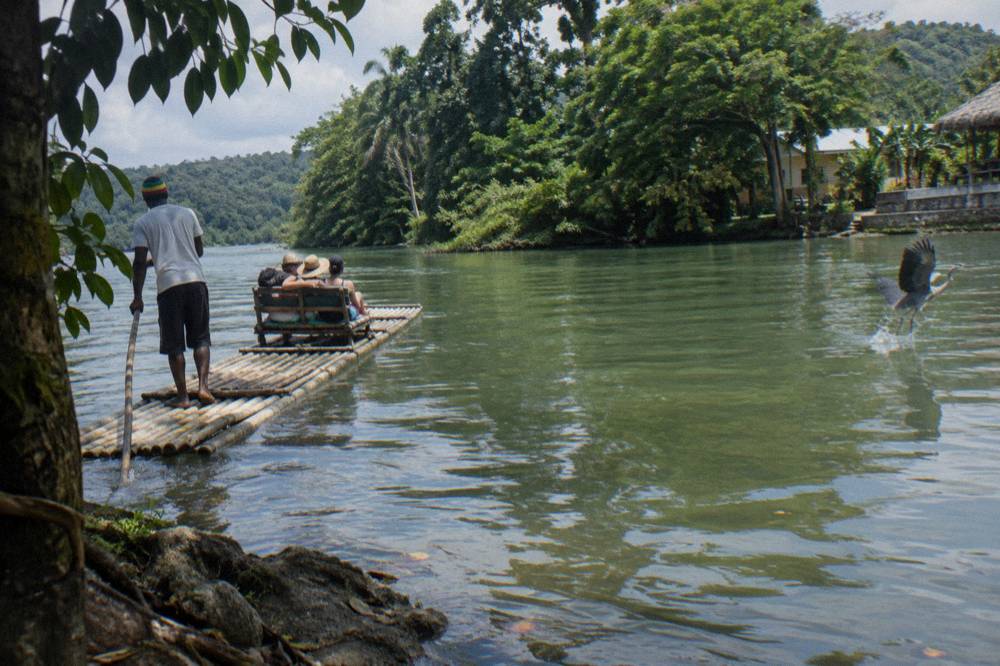 A bamboo raft poled by its captain across calm green water reflecting trees