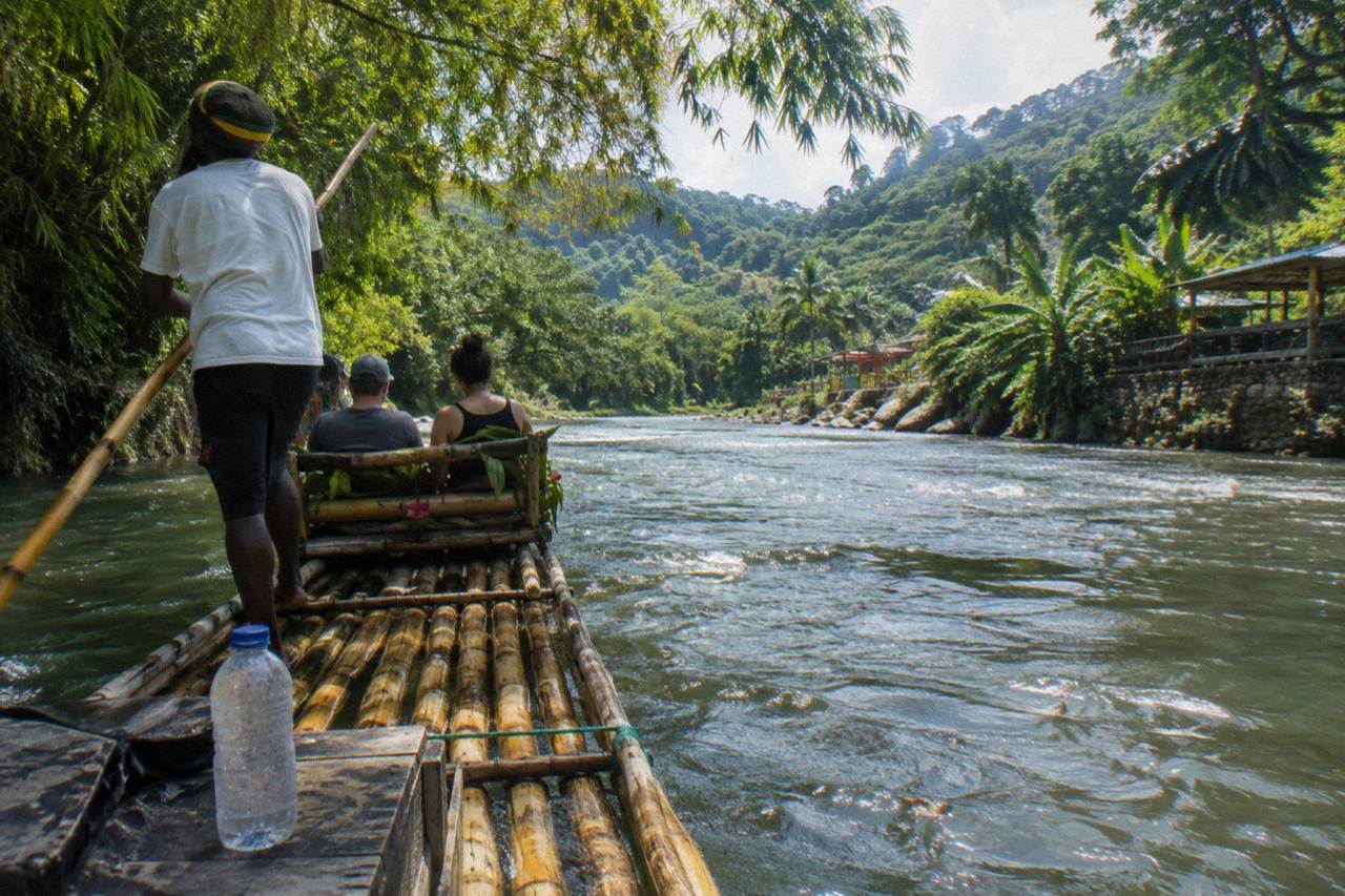 A long bamboo raft floating on a calm green river between tree covered banks