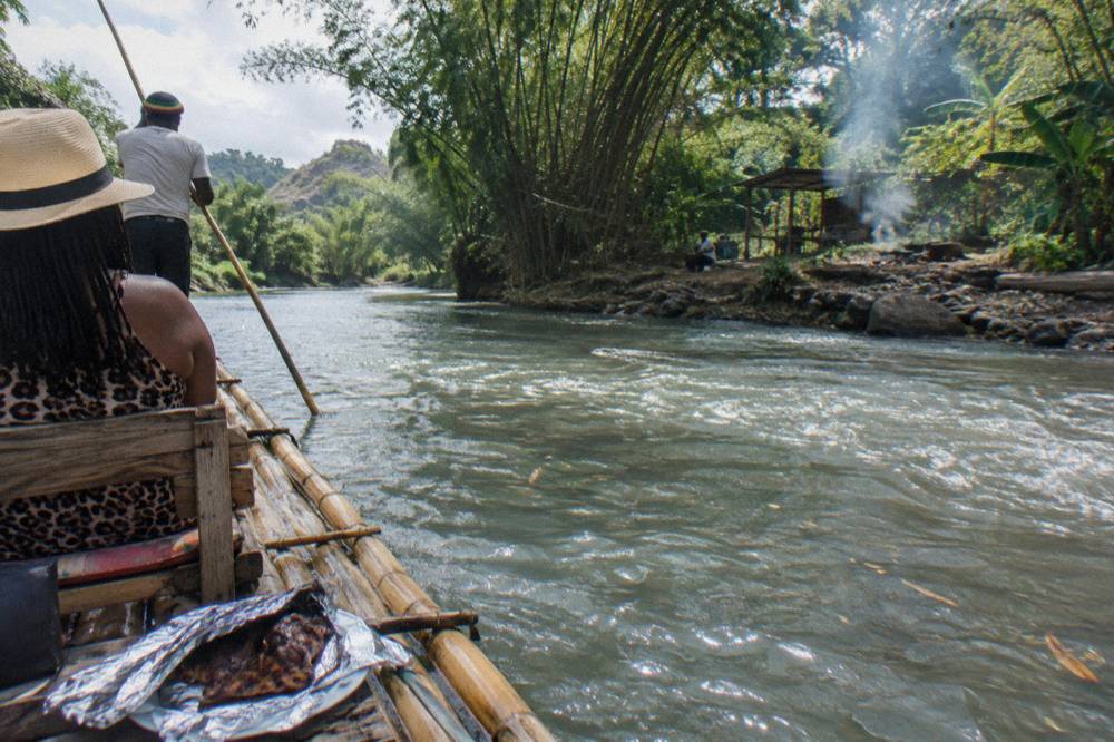 A bamboo raft on the Rio Grande with two passengers, a poling captain, and jerk chicken on the deck