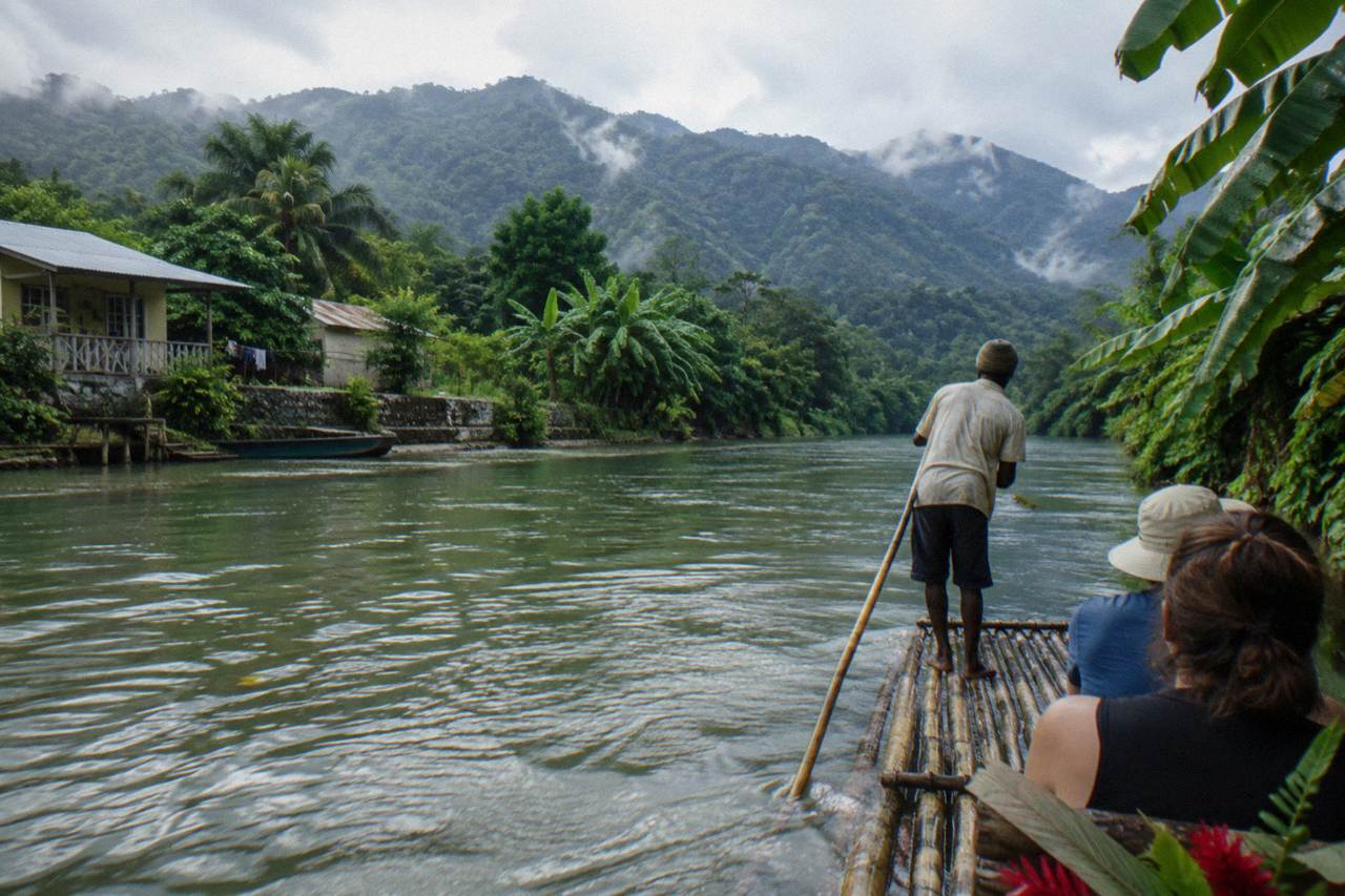 A bamboo raft drifting on a calm green river between forested banks in eastern Jamaica