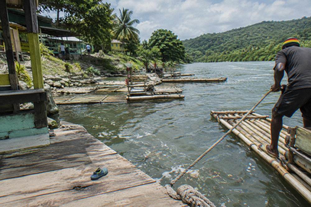 A river landing where several bamboo rafts wait in calm shallow water beside a wooden dock