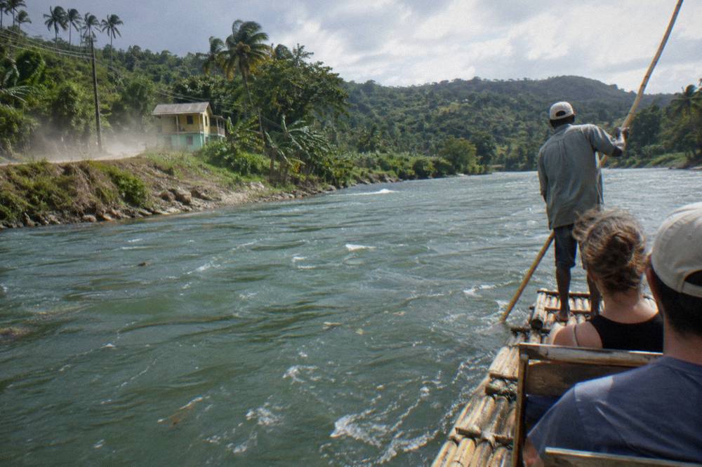 A bamboo raft captain standing at the rear of a raft poling along a wide calm river
