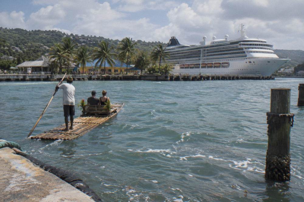 A cruise ship at a Caribbean pier with palm trees along the waterfront