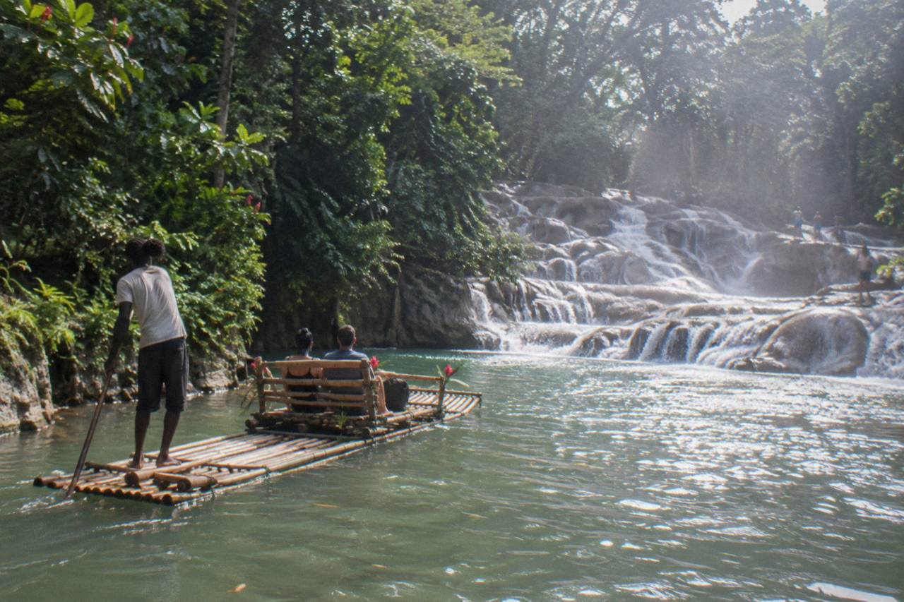 A bamboo raft resting on a calm green river with forested banks under a bright sky