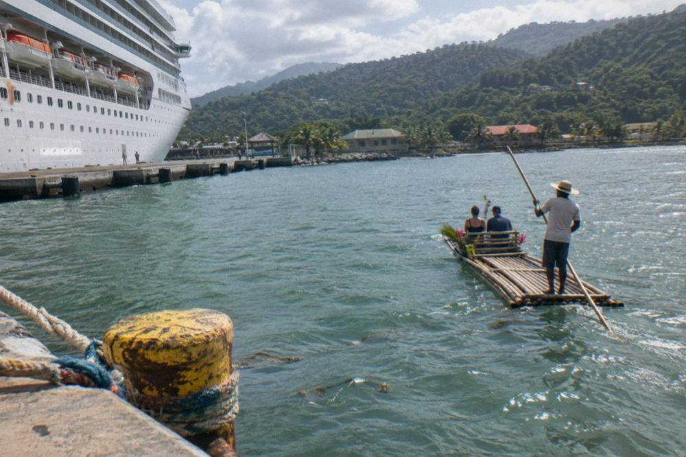 A cruise ship docked at a Caribbean pier with forested hills behind it