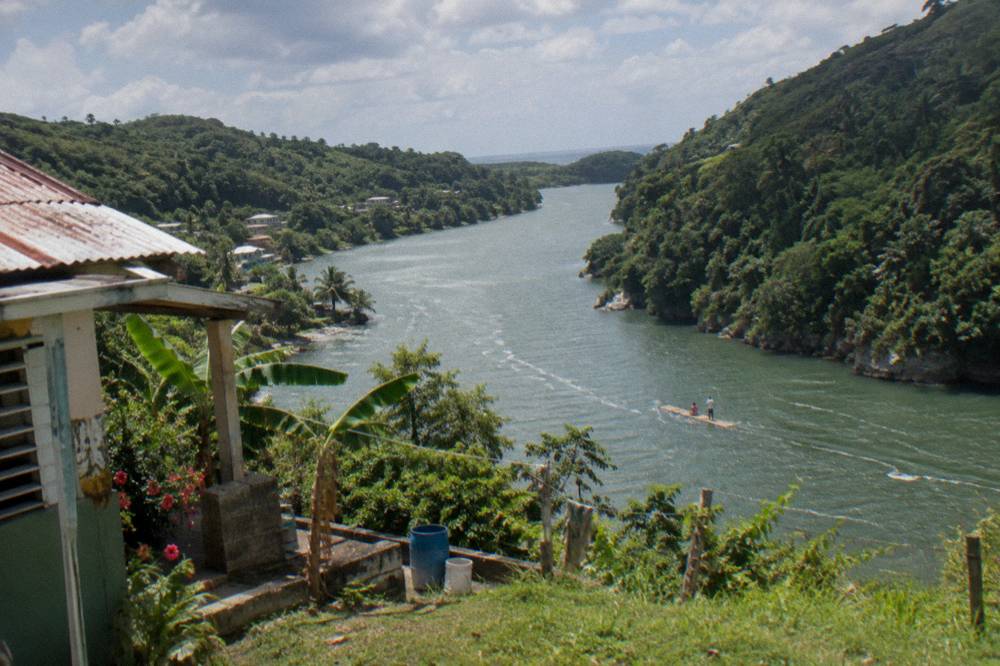A forested river valley with hills rising steeply on both sides under a partly cloudy sky