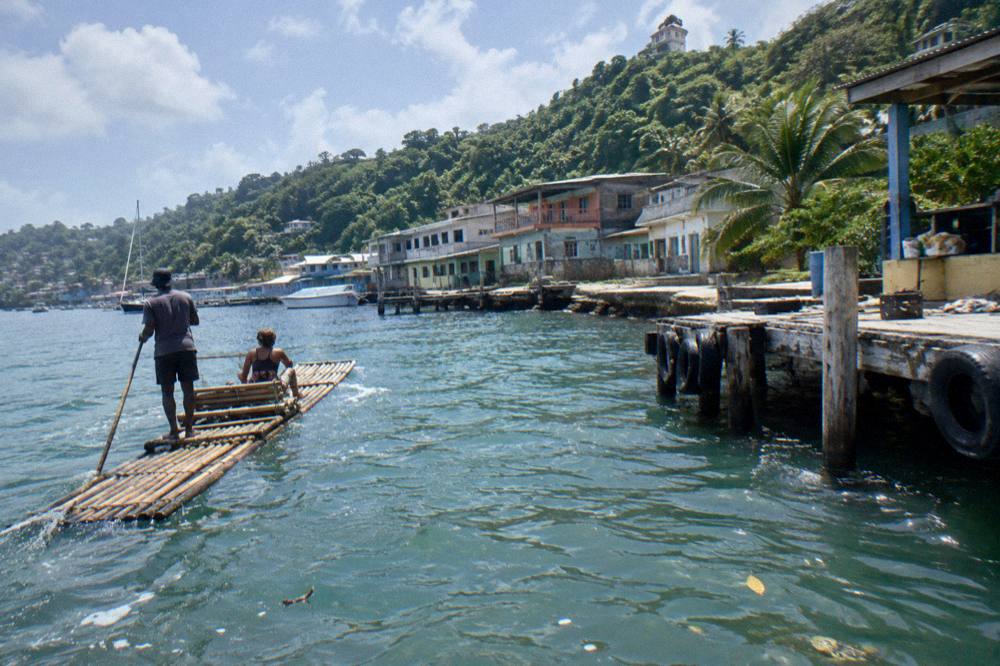 A coastal town beside a harbor with green hills rising behind small buildings