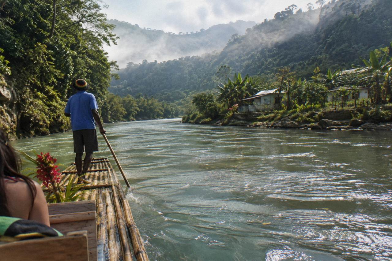 A long bamboo raft drifting on a calm green river between forested Jamaica hillsides