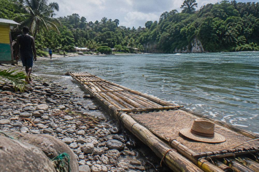 A bamboo raft resting on a riverbank beside calm green water and dense forest