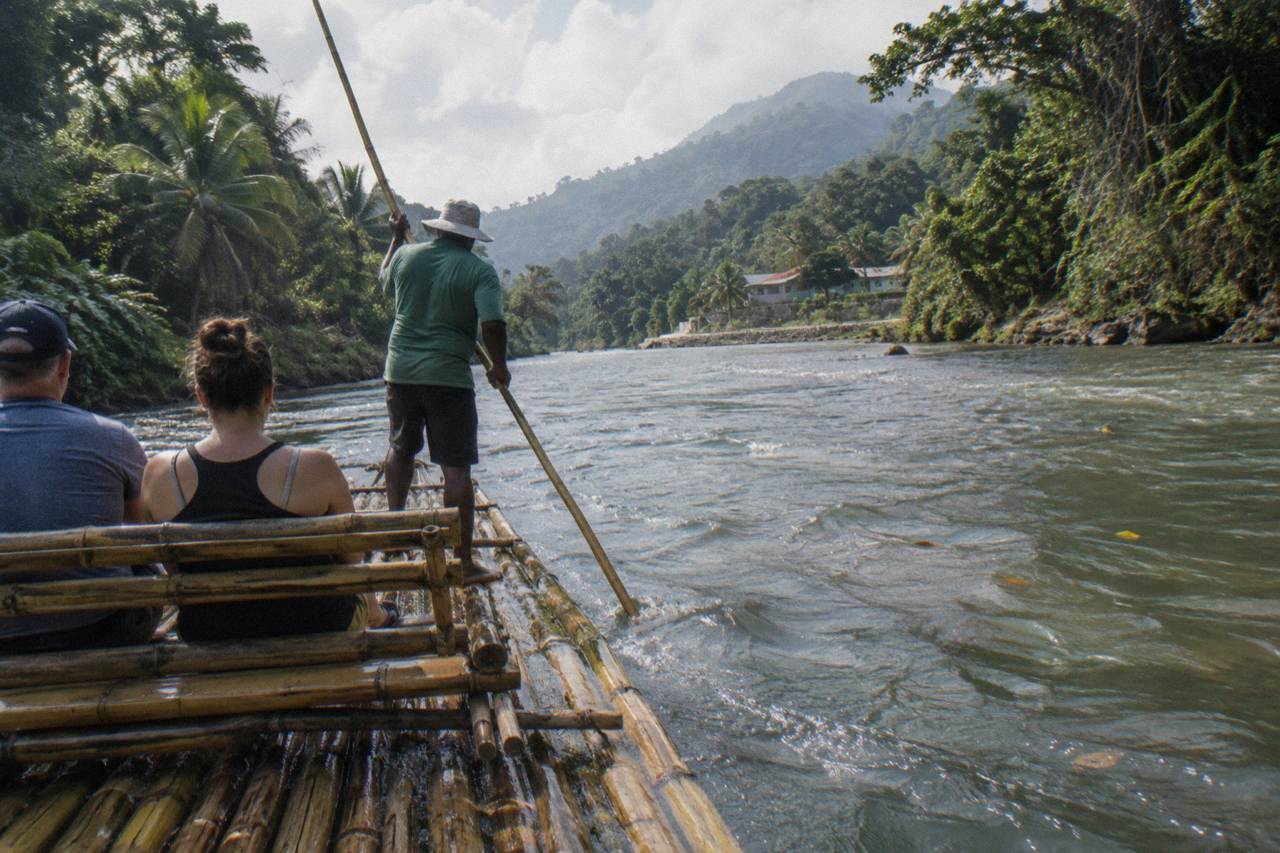 A long bamboo raft poled by a captain drifting between forested banks on a calm green river