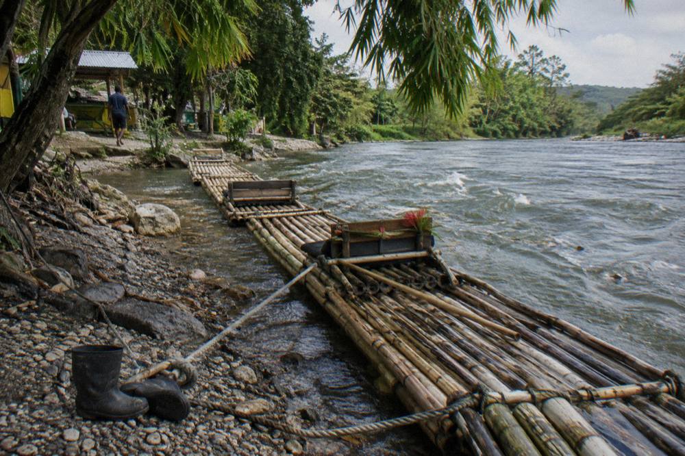 Two bamboo rafts tied at a river bank beside overhanging tropical trees
