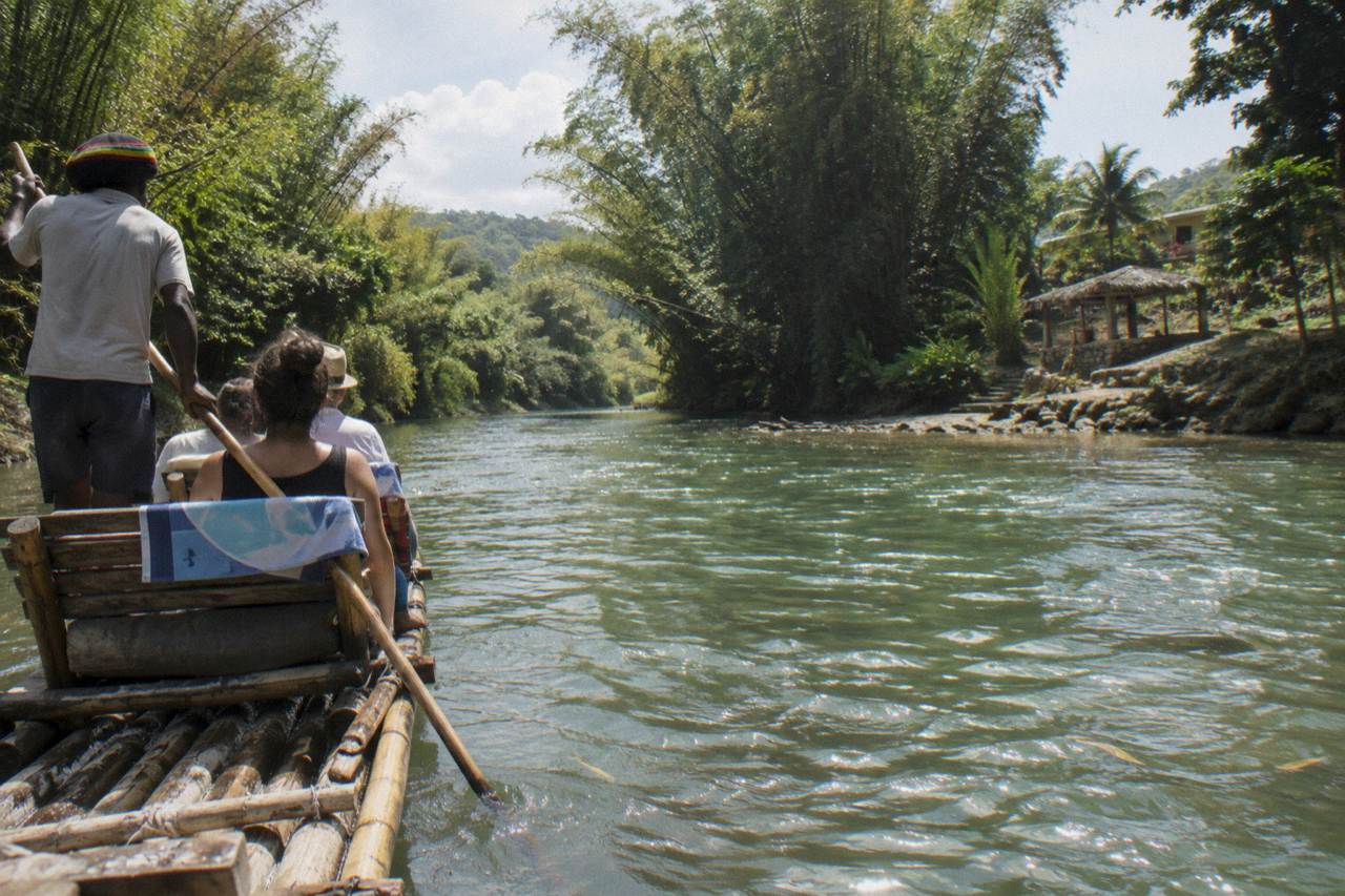 A long bamboo raft floating on calm green river water between forested banks in Jamaica