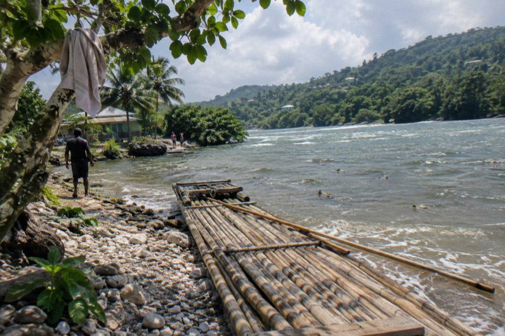 A wooden landing spot on a riverbank with a bamboo raft pulled up alongside