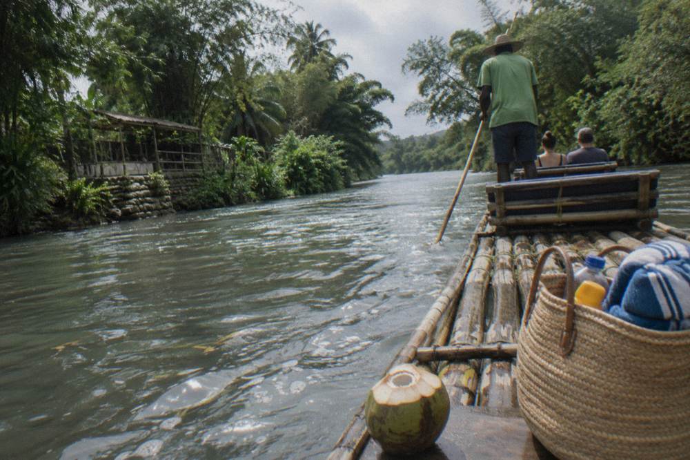 Bamboo raft on a Jamaican river, captain poling two passengers past dense bamboo banks