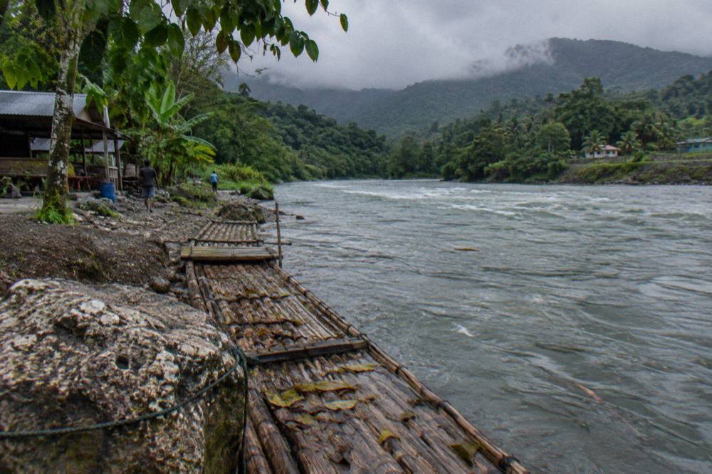 Low clouds passing over a green Jamaican river valley with a bamboo raft moored at the bank