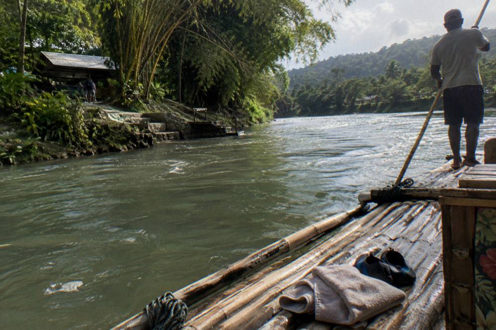 A dry towel and water shoes folded beside a bamboo raft at a quiet river landing
