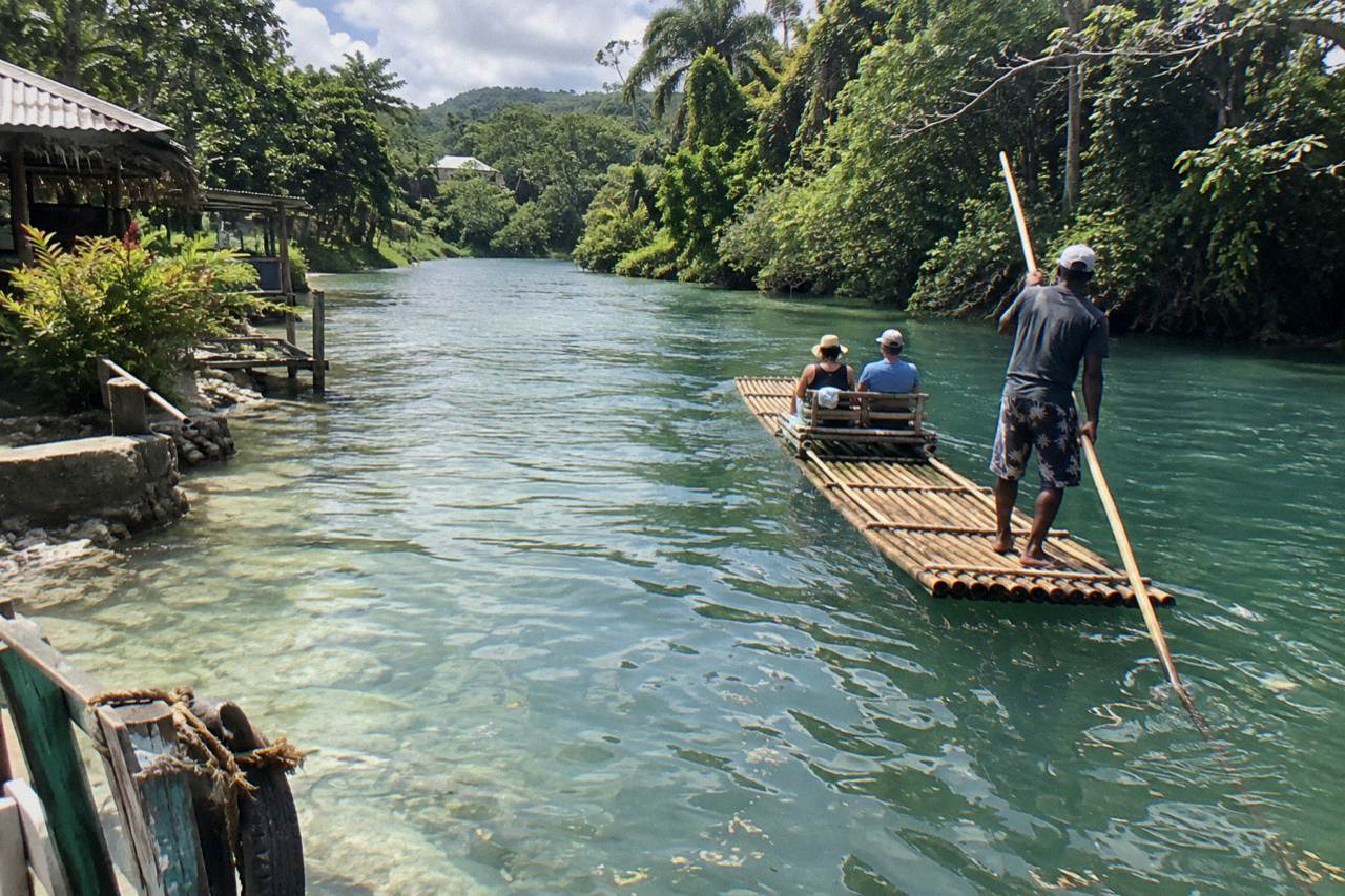 A long bamboo raft resting on a calm Jamaican river with dense green trees along both banks