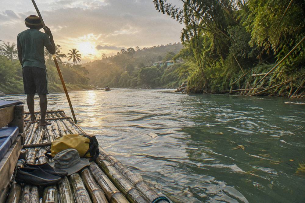 Water shoes, a hat and a dry bag arranged on a wooden bench beside a river