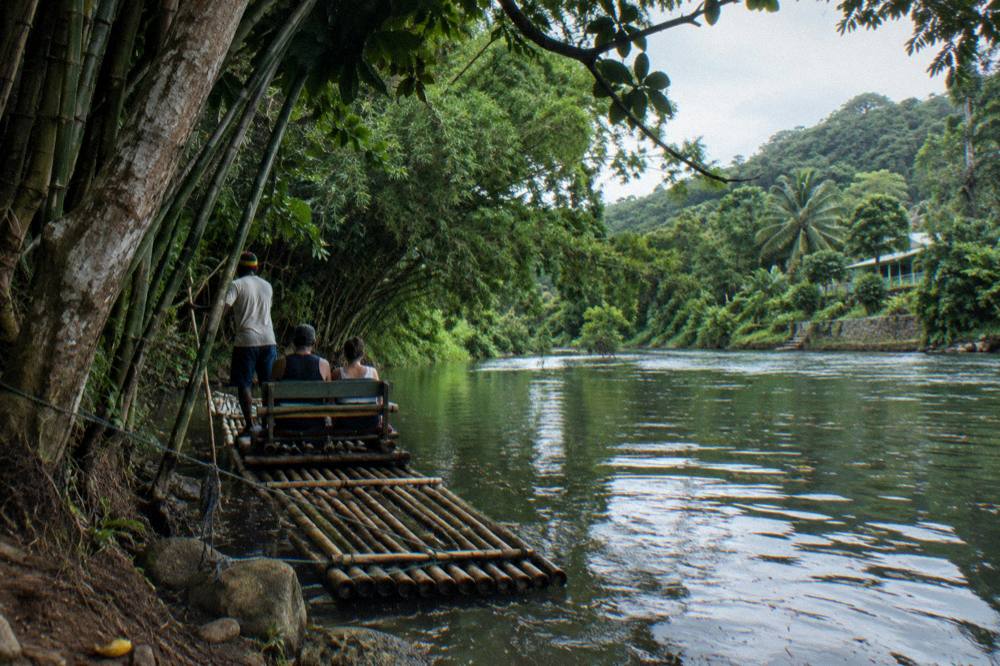 A calm river bend with bamboo raft moored in the shade of tall trees