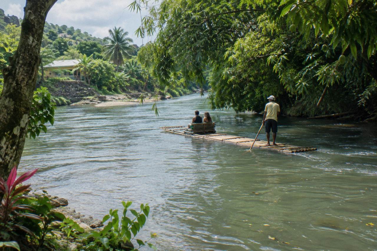 A long bamboo raft floating on a calm green river between overhanging trees on the White River near Ocho Rios